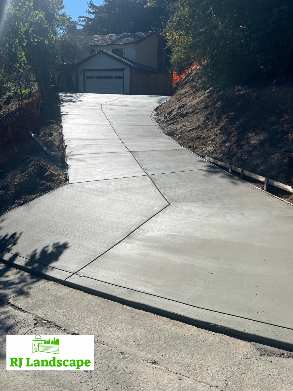 Completed concrete driveway installation by RJ Landscape, with the broad finished surface and hillside grade visible
